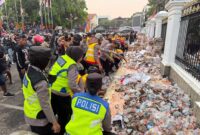 Anggota kepolisian membantu membersihkan sampah usai aksi unjuk rasa di Pati (foto:ist)