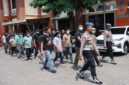 Petugas kepolisian menggandeng terduga para pelaku kasus bentrokan antara kelompok penagih utang dan warga di Desa Jepang, Kudus. Polisi masih mendalami peran masing-masing pihak dalam perkara tersebut. Foto: JP