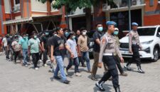 Petugas kepolisian menggandeng terduga para pelaku kasus bentrokan antara kelompok penagih utang dan warga di Desa Jepang, Kudus. Polisi masih mendalami peran masing-masing pihak dalam perkara tersebut. Foto: JP