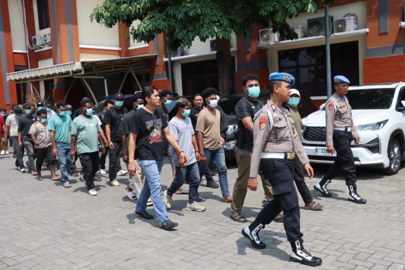 Petugas kepolisian menggandeng terduga para pelaku kasus bentrokan antara kelompok penagih utang dan warga di Desa Jepang, Kudus. Polisi masih mendalami peran masing-masing pihak dalam perkara tersebut. Foto: JP